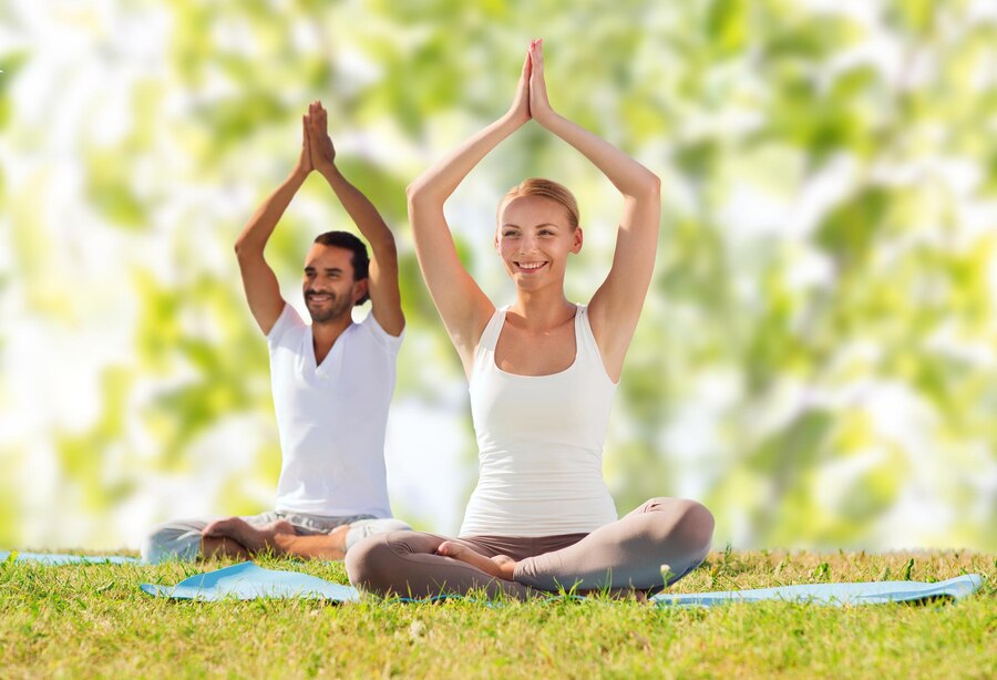 sport fitness yoga people concept smiling couple meditating sitting mats with raised hands green tree leaves background